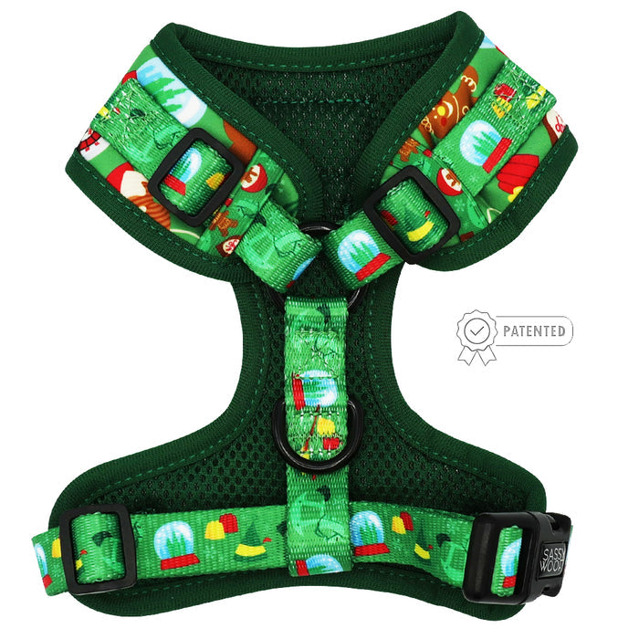 The Sassy Woof Dog Adjustable Harness - Elf™ is a green no pull harness with cartoon holiday patterns like snow globes and trees, black buckles, metal rings, mesh padding, and a PATENTED icon.