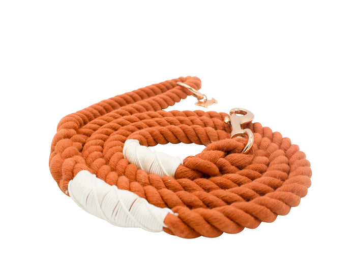 The Sassy Woof Dog Rope Leash - Athens features a thick, coiled orange cotton rope with white wrapped accents and a rose gold clasp, shown on a white background.
