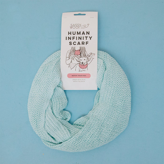 A light blue Sassy Woof Human Infinity Scarf is arranged in a loop on a blue background. The label reads "Human Infinity Scarf - Blue" by Sassy Woof—a cozy cold-weather accessory perfect for stylish duos.