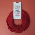 The Sassy Woof Human Infinity Scarf - Red is displayed in a circle on a red background with its branded tag, making it perfect for cozy cold weather walks with your pup.