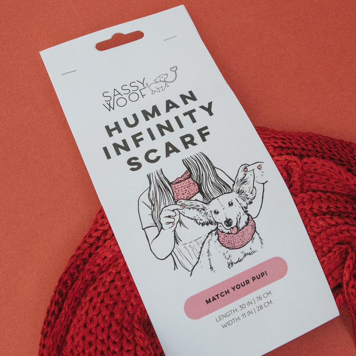 Product tag for Sassy Woof Human Infinity Scarf - Red, featuring an illustration of a woman and her dog, both in matching scarves against a red background. Includes scarf dimensions—perfect for cold weather.